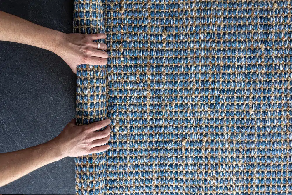 Hand unrolling blue and natural woven area rug on dark floor. Professional Johns Creek, GA Carpet Installation services.