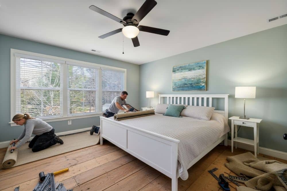 Professional contractors performing a Chamblee, GA carpet installation in a modern bedroom with hardwood subflooring.